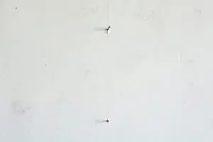 Common causes of nail pops in painted walls showing raised drywall fasteners pushing through a white interior wall