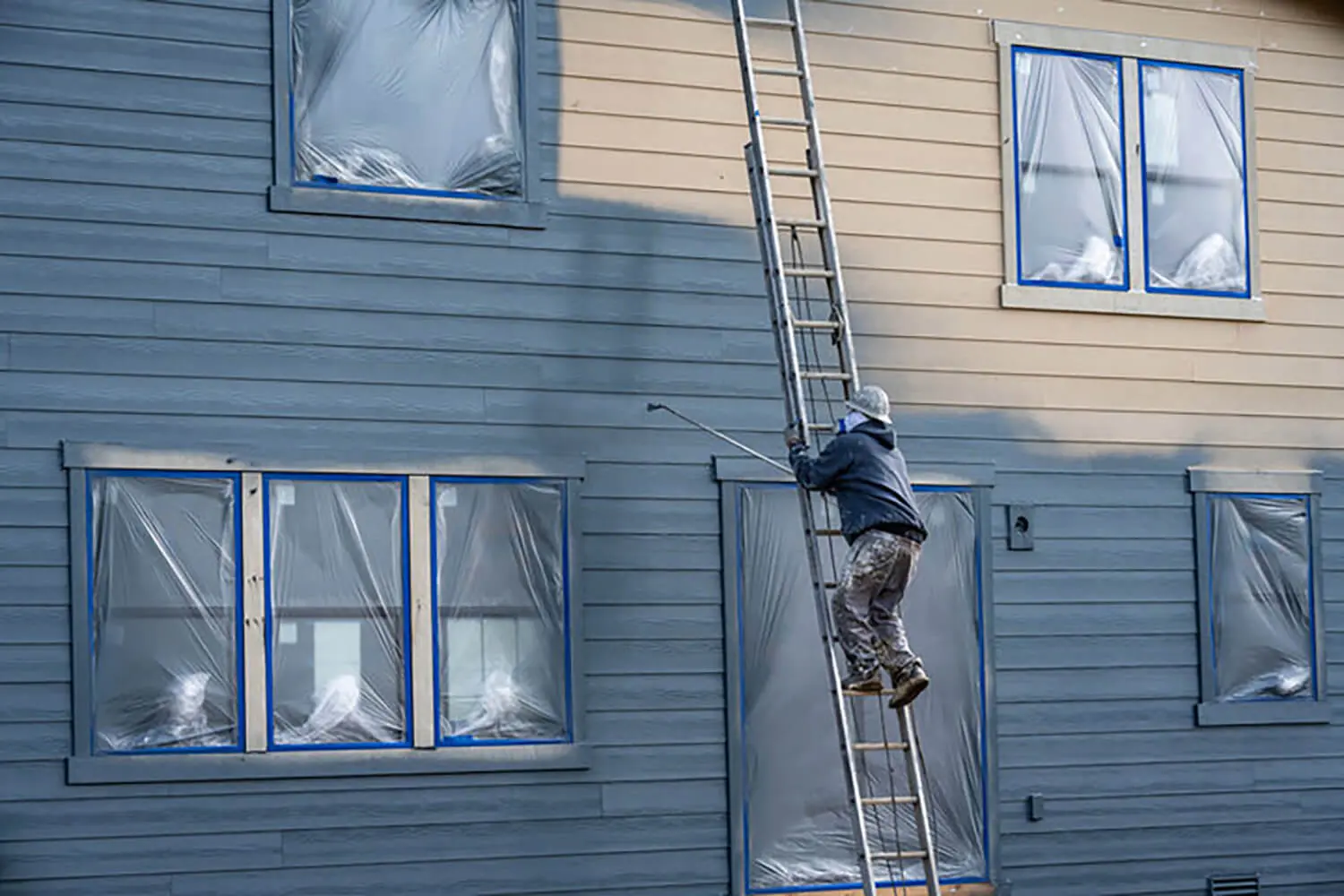 Exterior painter on ladder inspecting siding to show how winter damage shows up on exterior paint surfaces through peeling and wear