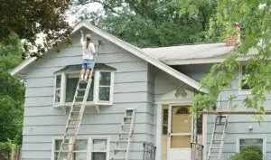 Homeowner on ladder painting house exterior, illustrating when should you start planning exterior painting in Whitby