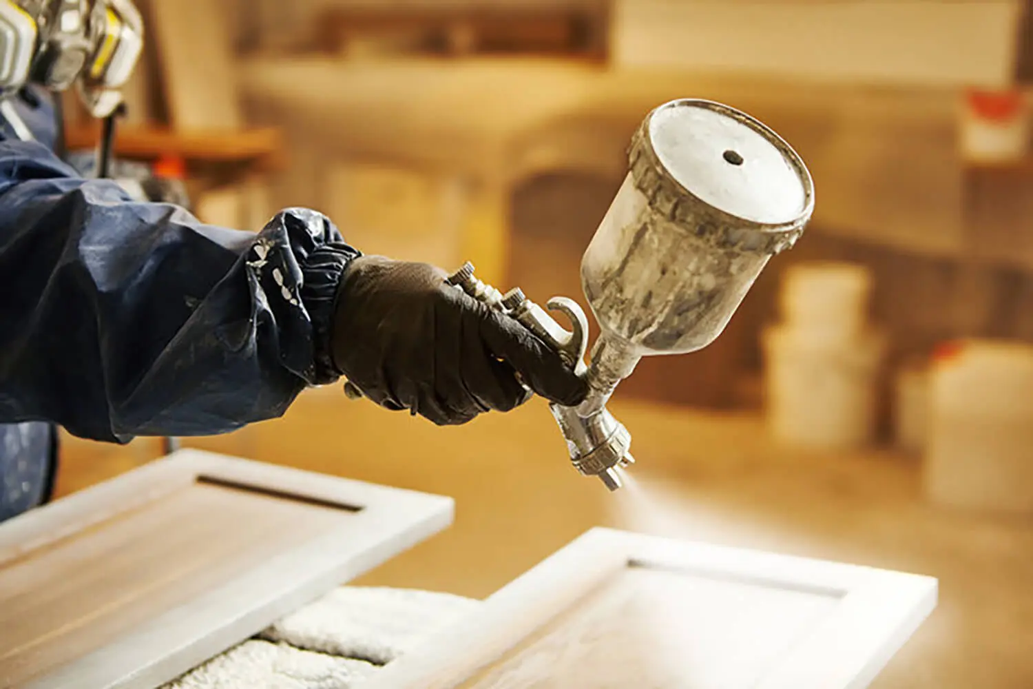 Professional painter spraying kitchen cabinet doors during refinishing, showing when cabinet painting is a better option than replacement