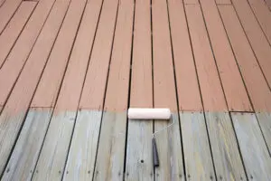 A deck being repainted, showing weathered bare wood on one side and freshly applied paint on the other, illustrating signs a deck needs to be repainted.