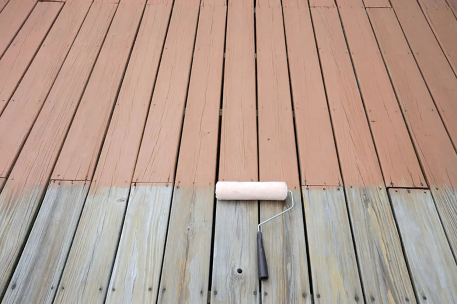 A deck being repainted, showing weathered bare wood on one side and freshly applied paint on the other, illustrating signs a deck needs to be repainted.