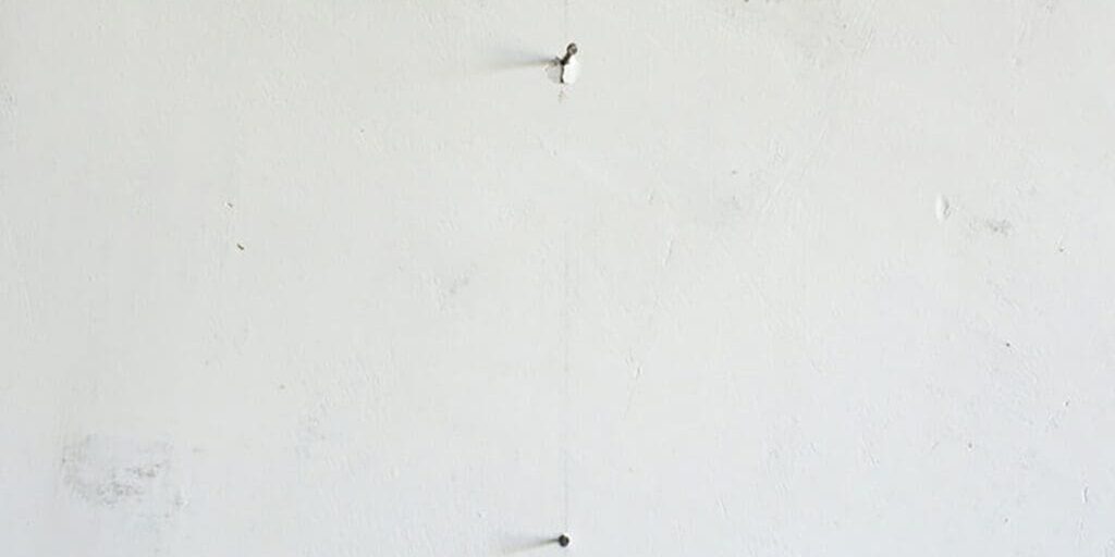 Common causes of nail pops in painted walls showing raised drywall fasteners pushing through a white interior wall