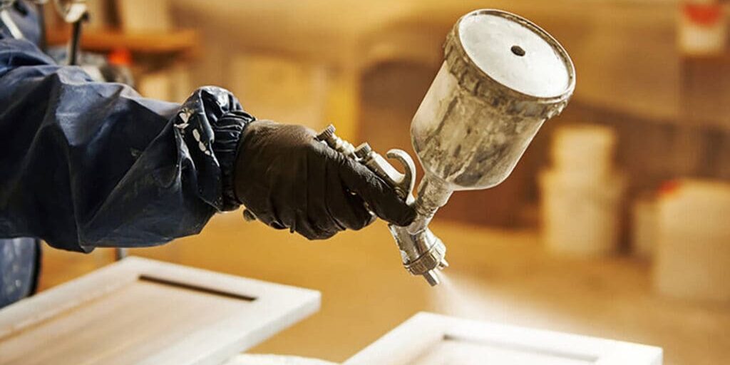 Professional painter spraying kitchen cabinet doors during refinishing, showing when cabinet painting is a better option than replacement